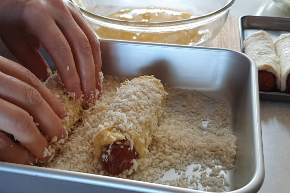 Pressing bread crumbs onto rolled bread corn dogs
